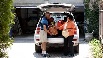 A couple unloads groceries from the back of their SUV.